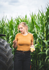 Maisanbau - junge Landwirtin vor einem Maisfeld freut sich über gut entwickelte Maiskolben.
