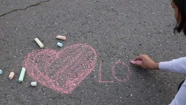 A woman drawing a heart and word LOVE with a chalk on asphalt. Drawings paintings on asphalt