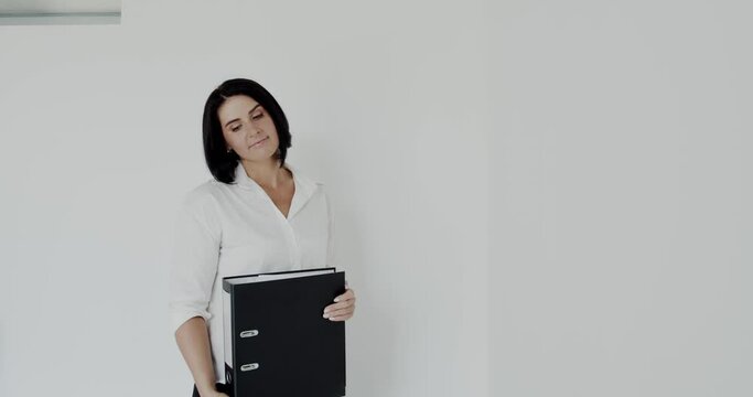 Happy teacher with black folder in hands poses with smile at camera in office