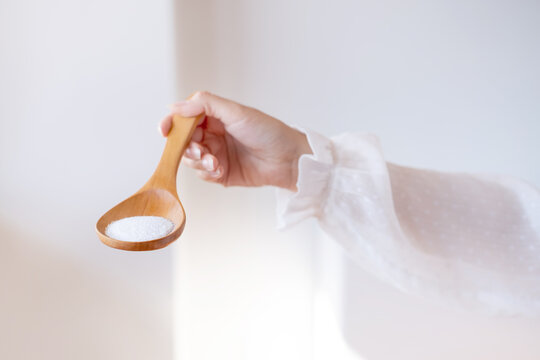 Woman in white blouse holding in hand wooden spoon with magnesium or calcium supplement powder. Bioa