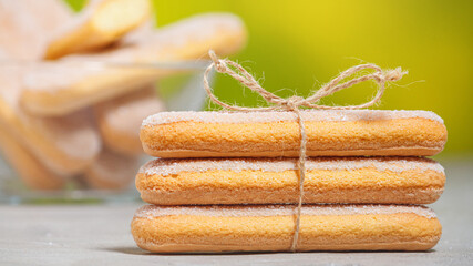 Traditional Italian savoiardi or ladyfingers cookies on a stack tied with a rope. Biscuits in a glass bowl in the background. Selective focus