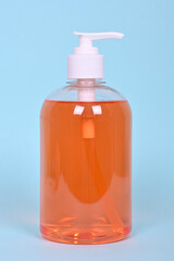 A bottle of orange liquid soap on a blue background.