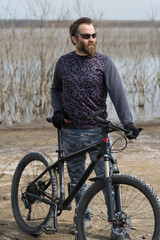 Sports brutal bearded guy on a modern mountain bike. A cyclist in a salt deserted place by the lake.