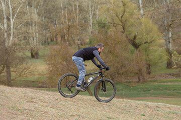 Fototapeta na wymiar Sports brutal bearded guy on a modern mountain bike. Cyclist on the green hills in the spring.