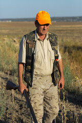 Duck hunter with shotgun walking through a meadow.
