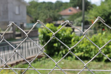 Grillage de banlieue derrière lequel on distingue de la verdure estivale.