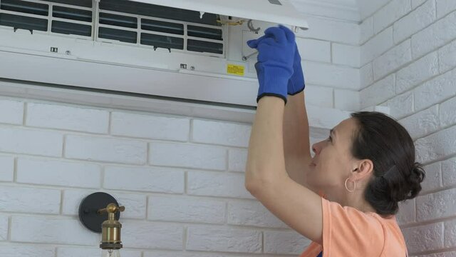 Repair the air conditioner. A woman with a tool twist the screw from the air conditioner.
