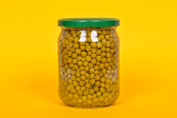 Canned green peas in a glass jar on a yellow background.