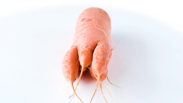 Ugly carrot rotate on a white background. Funny, unnormal vegetable or food waste concept. Horizontal orientation
