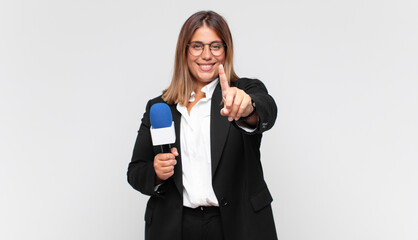 young woman reporter smiling proudly and confidently making number one pose triumphantly, feeling...