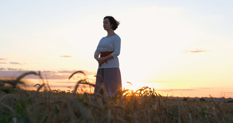Fototapeta na wymiar Female practicing qigong in summer fields with beautiful sunset on background 