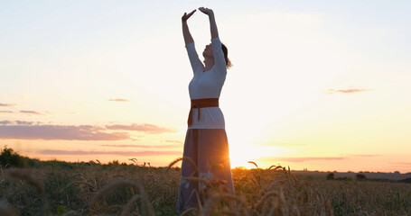 Female practicing qigong in summer fields with beautiful sunset on background	
