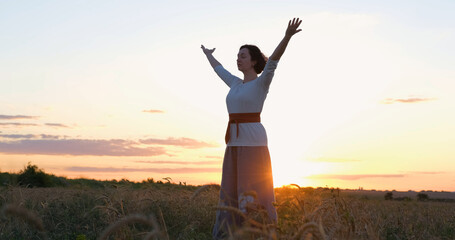 Female practicing qigong in summer fields with beautiful sunset on background	