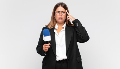 young woman reporter looking surprised, open-mouthed, shocked, realizing a new thought, idea or...