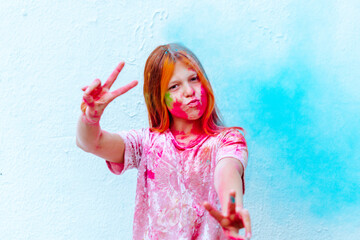 happy girl painted with Holi festival pink and blue colours on white wall background