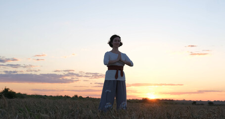 Female practicing qigong in summer fields with beautiful sunset on background	