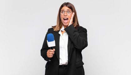 young woman reporter feeling happy, excited and surprised, looking to the side with both hands on...