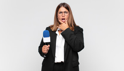 young woman reporter with mouth and eyes wide open and hand on chin, feeling unpleasantly shocked,...