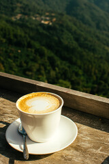 Hot latte coffee in winter morning at hillside with mountain background. Copy space for text.
