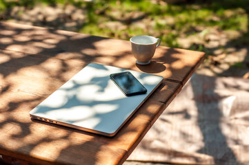 View on a closed laptop pc and a smartphone and a mug on a table in the garden