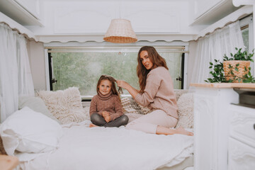 Happy family - mother and little daughter relaxing hugging and having fun in countryside inside white scandinavian rustic camper van interior. Domestic tourism concept.