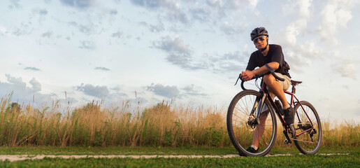Fototapeta na wymiar Cyclist sits on a gravel bicycle in a field at the golden hour. Active lifestyle concept. Copy space.