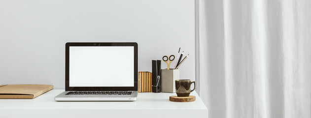 Desk with laptop mockup coffee mug and grey curtain.