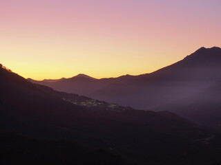 Mountain valley with houses glowing in the distance against a sunset