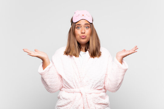 young woman wearing pajamas, feeling puzzled and confused, doubting, weighting or choosing different options with funny expression
