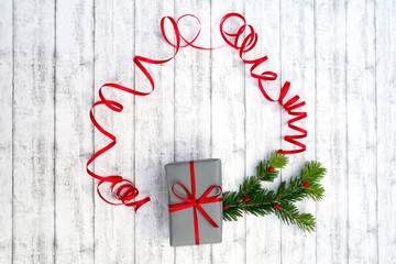 Weihnachtshintergrund, Rahmen aus rotem Geschenkband mit Schwung, Platz für Text, grüner Zweig, Geschenk grau, weißes Holz, Beeren, Früchte.