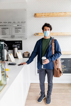 Portrait confident young man in face mask holding coffee in cafe