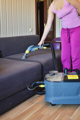 Close up of a woman cleaning sofa at home with vacuum cleaner