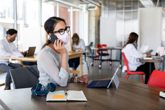 Woman in face mask using phone in socially distanced coworking space