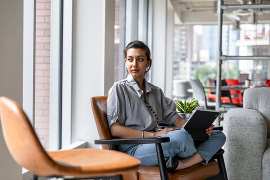 Woman Looking Away From Digital Tablet In Business Coworking Space