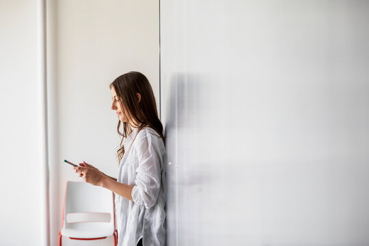 Woman using phone against white wall in office