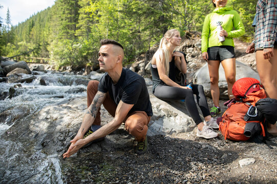 Young Male Hiker Washing Hands At Stream In Woods