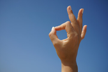 beautiful female hand demonstrates the symbol OK okay against the background of a clear blue sky on a clear sunny day