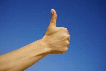 beautiful female hand demonstrates the symbol OK okay against the background of a clear blue sky on...