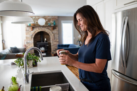 Smiling Woman Opening Jar At Kitchen Sink