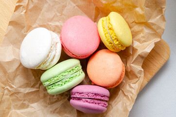 many multicolored crunchy delicious macarons on craft paper for baking on gray concrete background. morning coffee concept. sweets and desserts.