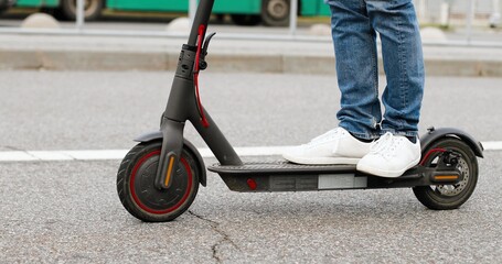 Close up of male feet in white sneakers standing on electric scooter an driding on road at city street. Man having fast ride in town. Modern vehicle. Urban transportation.