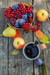 Copper mug with tea on a wooden old table with viburnum berries, plums, apples. Autumn still life in a rustic style.