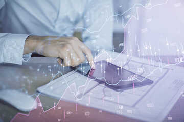 Double exposure of man's hands holding and using a digital device and forex graph drawing. Financial market concept.