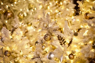 White snowy Christmas tree branches decorated with beautiful golden Christmas decorations, bright toys, sparkling garlands and balls. Festive Christmas lights and Magic decorations close-up.  