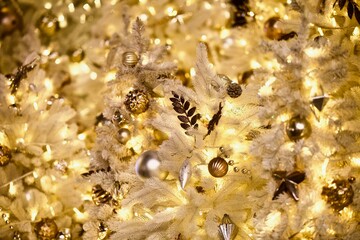 White snowy Christmas tree branches decorated with beautiful golden Christmas decorations, bright toys, sparkling garlands and balls. Festive Christmas lights and Magic decorations close-up.  