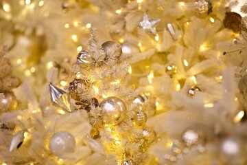 White snowy Christmas tree branches decorated with beautiful golden Christmas decorations, bright toys, sparkling garlands and balls. Festive Christmas lights and Magic decorations close-up.  