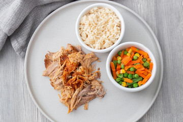 Pulled pork with rice and vegetables on a grey plate.  Grey wood background with a tea towel