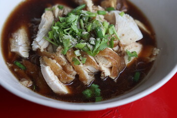 Thai style of chicken noodle with bitter gourd in white bowl on red table background. One of the most popular Thai street food dishes to try.