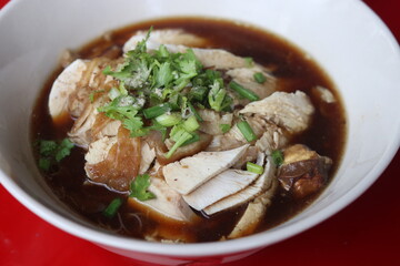 Thai style of chicken noodle with bitter gourd in white bowl on red table background. One of the most popular Thai street food dishes to try.