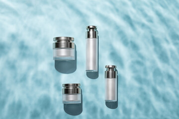 Top view of skincare bottles on a light blue water surface - obrazy, fototapety, plakaty